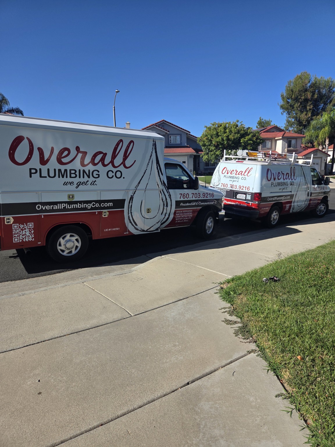 Two branded Overall Plumbing Co. service trucks at a customer property